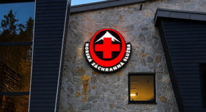 Exterior stone-clad wall of a building with a circular red cross sign and the text 'HOREKA ZACHRANNA SLUZBA'.