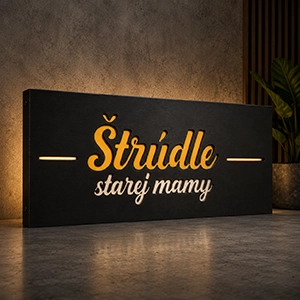 Black rectangular sign with gold cursive text reading 'Štrúdle starej mamy' in a warmly lit space.