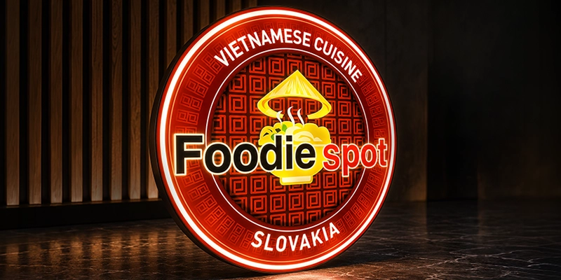 Circular neon sign with the 'Foodie spot' logo, advertising Vietnamese cuisine in Slovakia, featuring a steaming noodle bowl and a conical hat in the center.