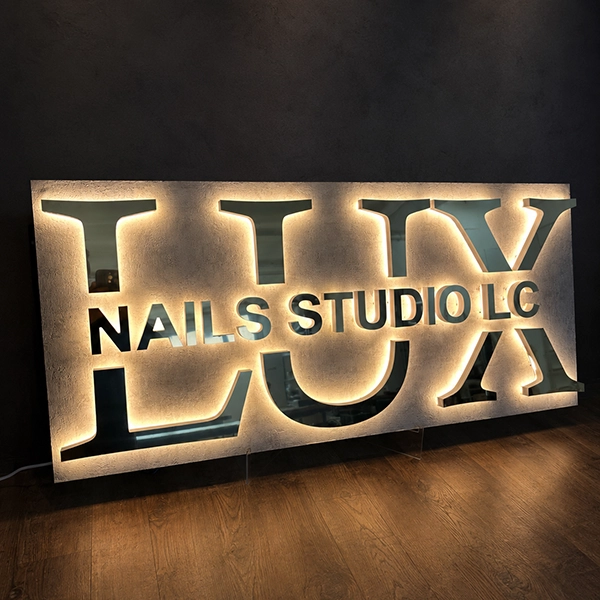 Illuminated sign reading 'LUX NAILS STUDIO LLC' in a dim room behind glass panels.